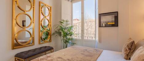 Quarto com uma cama grande, um banco e três espelhos fixados na parede.
