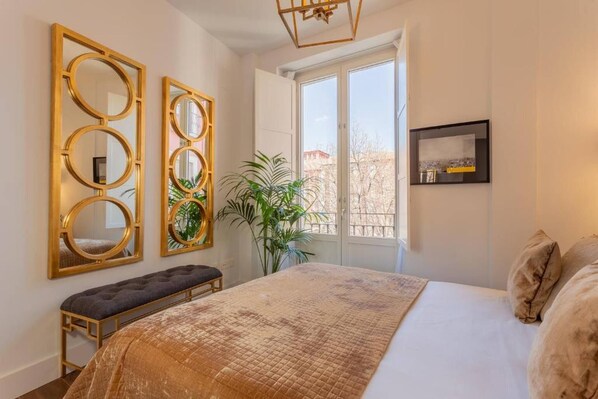 A bedroom with a large bed, a bench, and three wall-mounted mirrors. - Cathedral Royale Suite (granada)