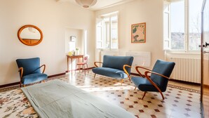 A spacious living room with a large window, a round mirror, and two blue armchairs. - Casa Dante in Lucca With 3 Bedrooms and 2 Bathrooms (Lucca)