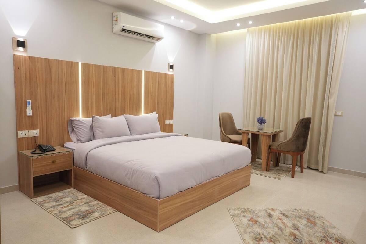 A modern hotel room with a wooden bed, bedside table, and a desk with two chairs.