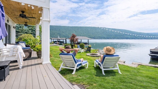 Eine Terrasse mit Liegestühlen, die auf einen See blickt, eine Laube und eine Lichterkette.