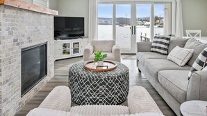 Ein modernes Wohnzimmer mit Kamin, Fernseher, einer Couch und Blick auf eine verschneite Landschaft durch große Fenster.