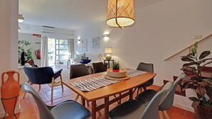 A dining area with a wooden table, black chairs, a woven pendant light, and a potted plant. - Marina Family Duplex with Pool (Loulé)