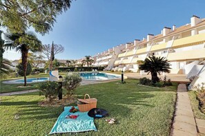 A poolside area with a grassy lawn, a picnic setup, and a row of white buildings with balconies. - Marina Family Duplex with Pool (Loulé)