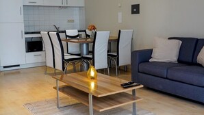 Moderni olohuone, jossa on puinen sohvapöytä, sininen sohva ja ruokailutila, jossa on valkoiset kaapit ja laatoitettu seinä ruokapöydän takana.
