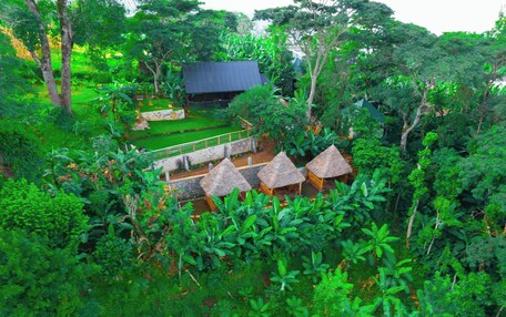 A lush, tropical garden with thatched-roof huts and a stone building.