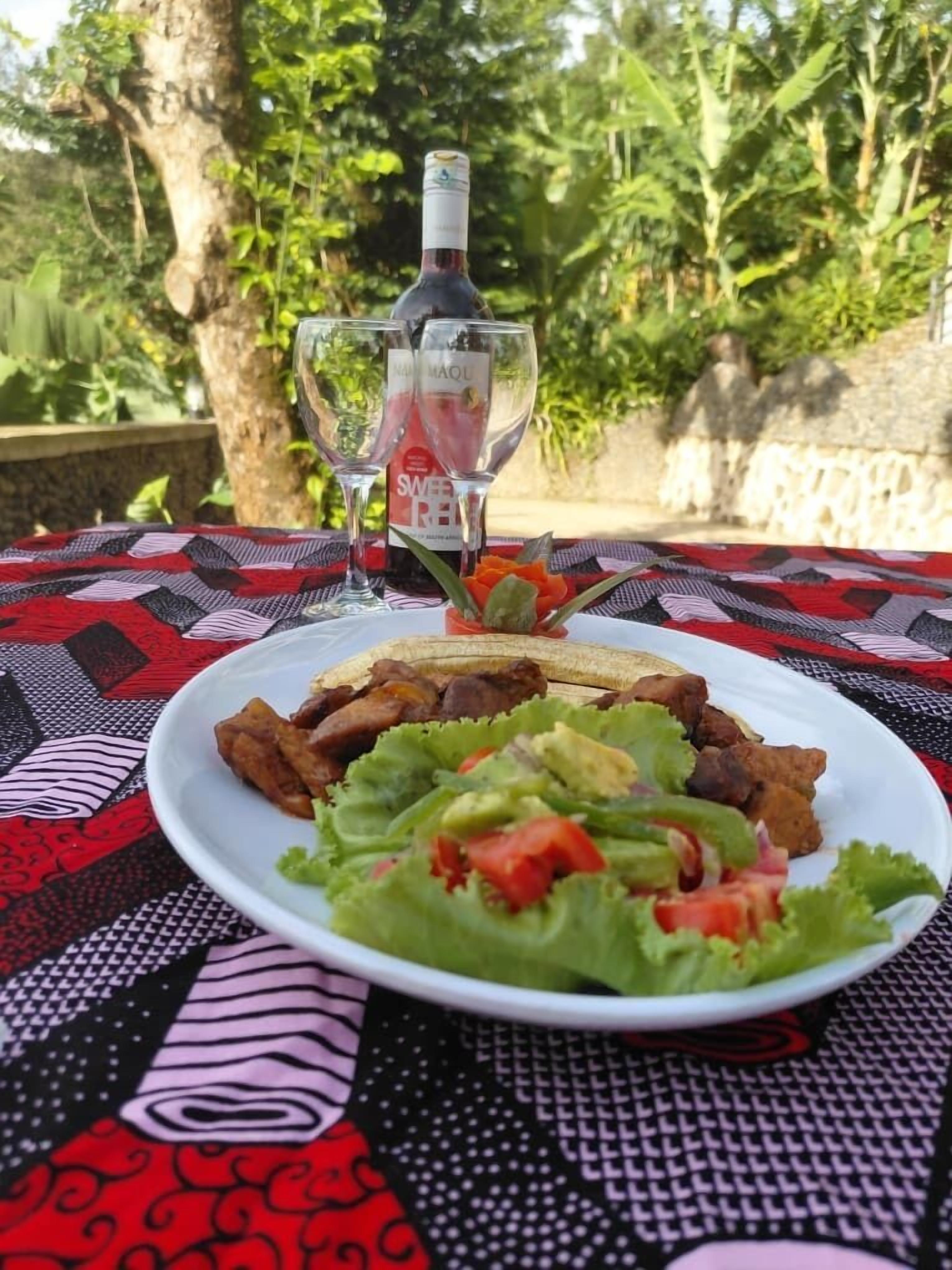 A plate of food with a bottle and glasses on a patterned tablecloth.