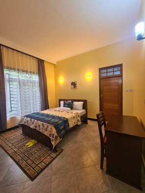 Une chambre à coucher avec un lit, un bureau et une chaise. Il y a deux lampes fixées au mur et une porte avec une fenêtre.