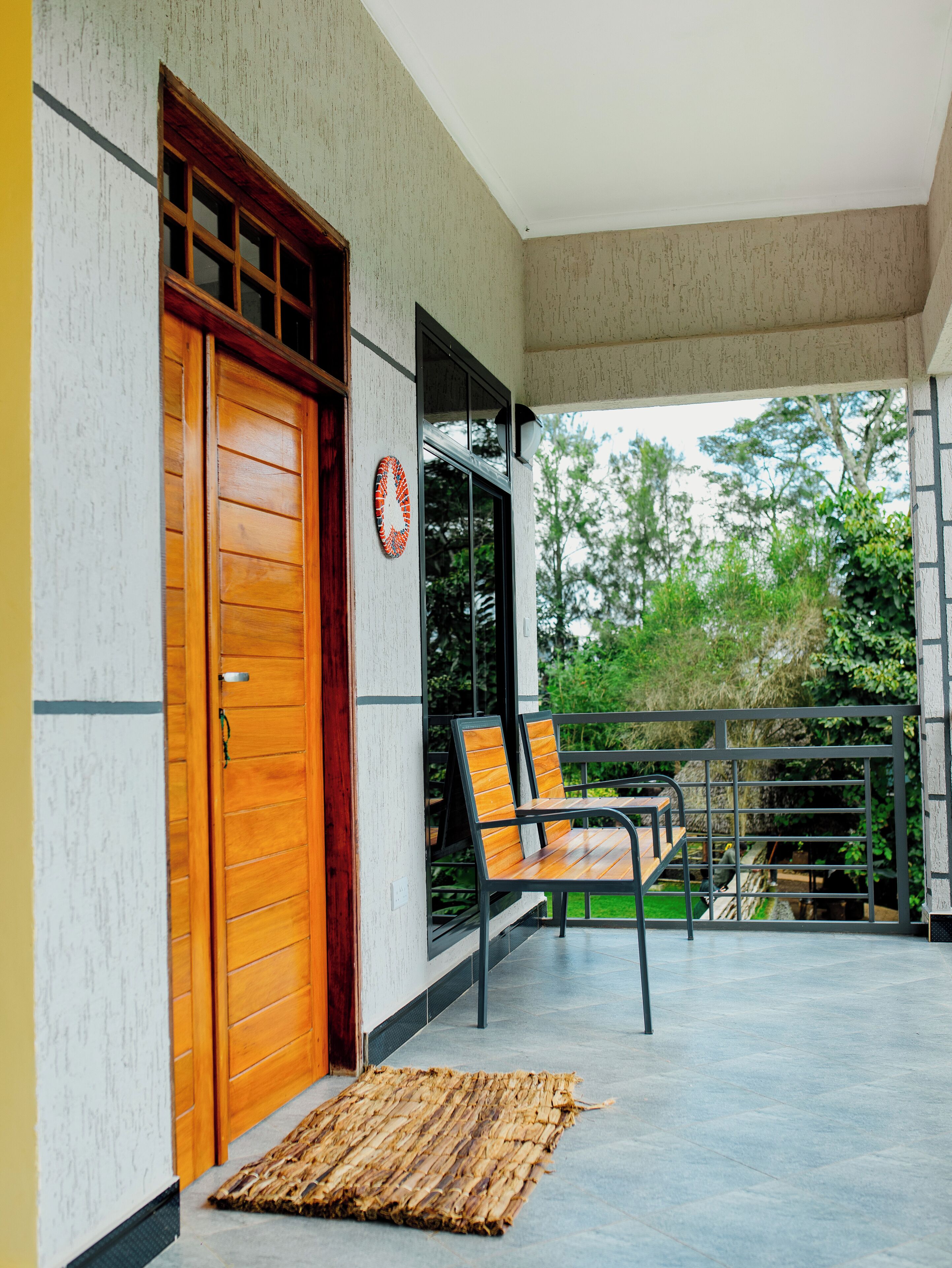 A covered outdoor seating area with a wooden door, a metal railing, and a view of greenery.