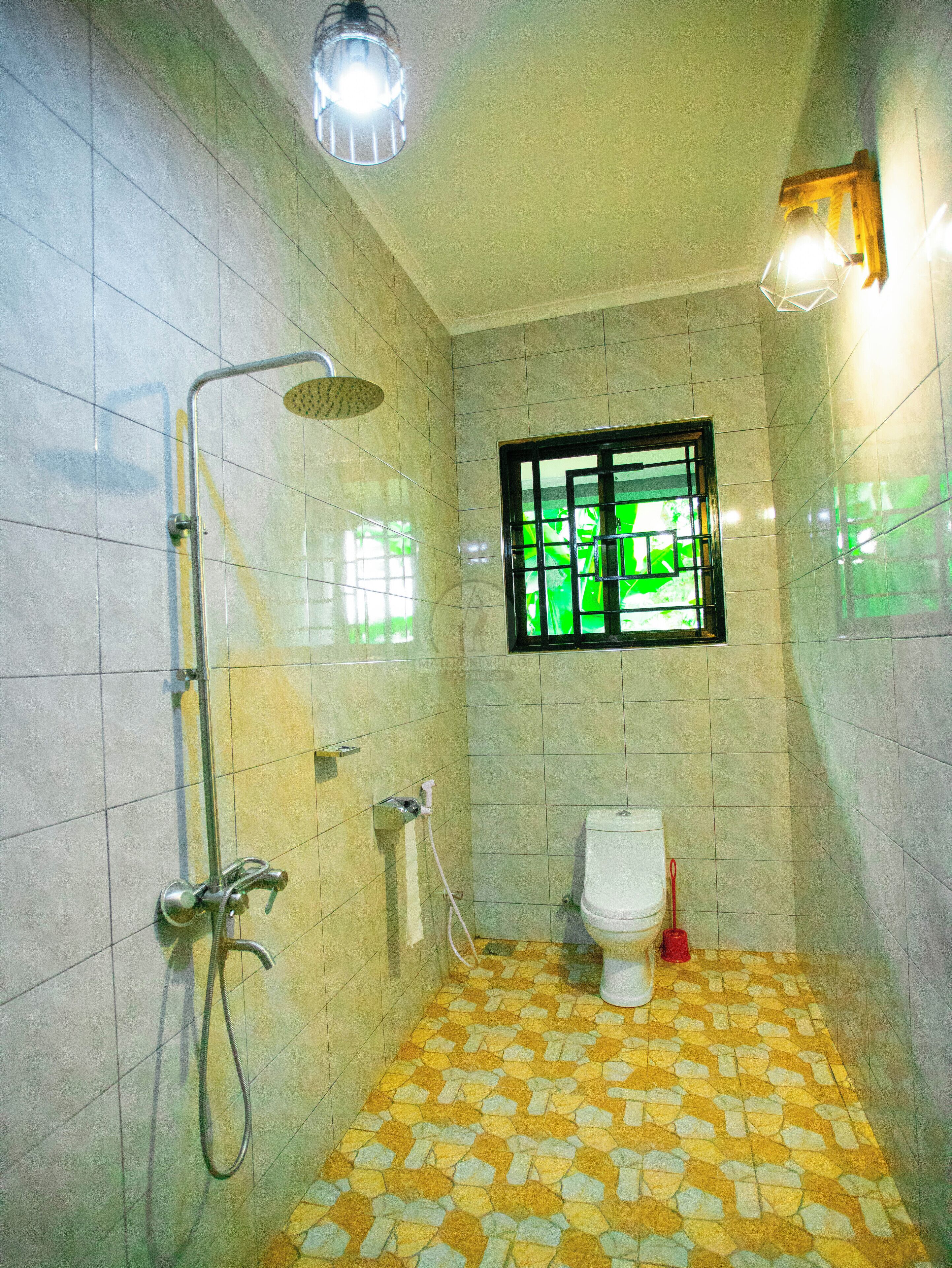 A bathroom with a shower, toilet, and a window with green foliage.