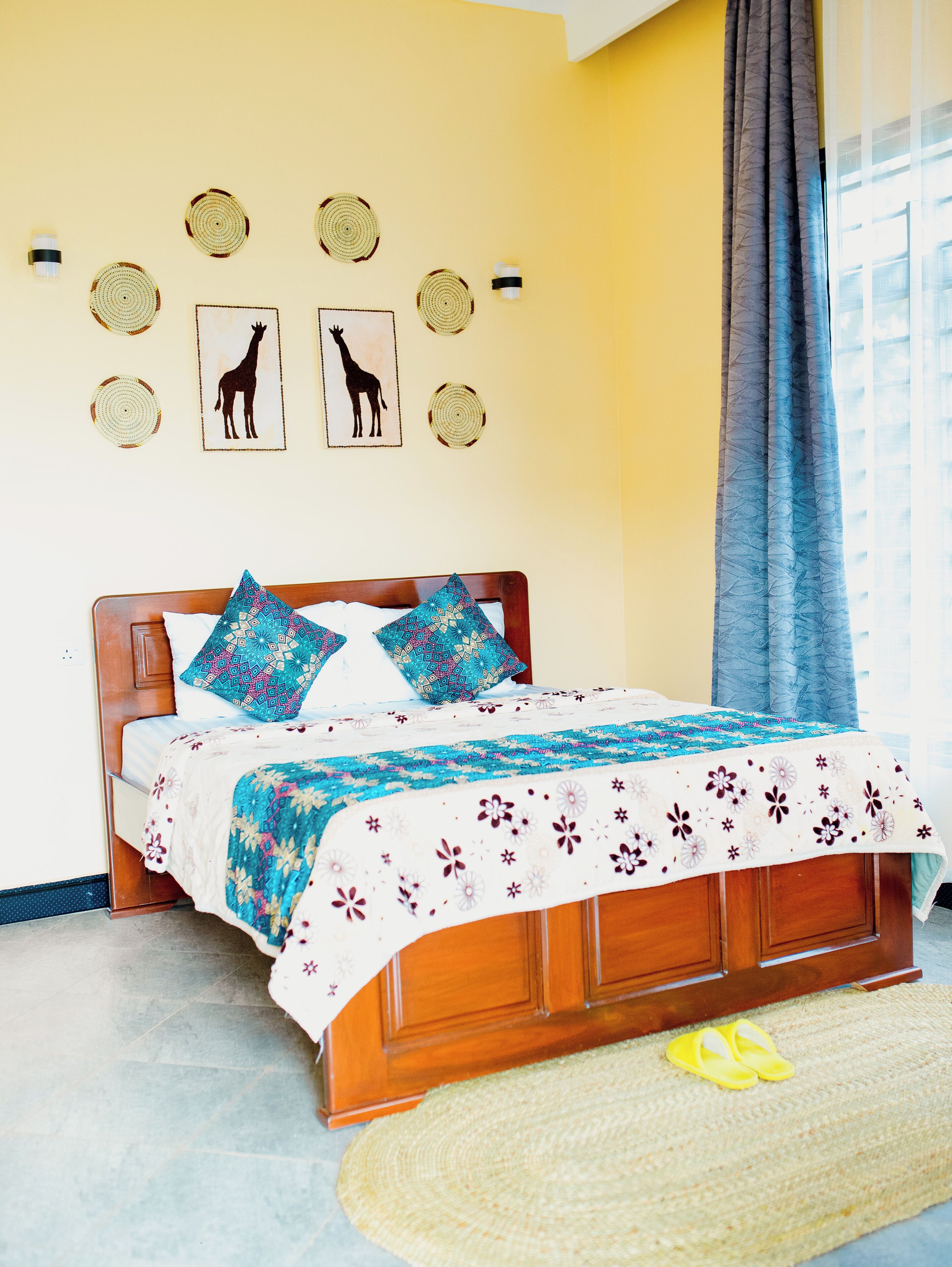 A bed with a patterned bedspread, a wooden headboard, and a wall with circular wall hangings and two framed pictures of giraffes.