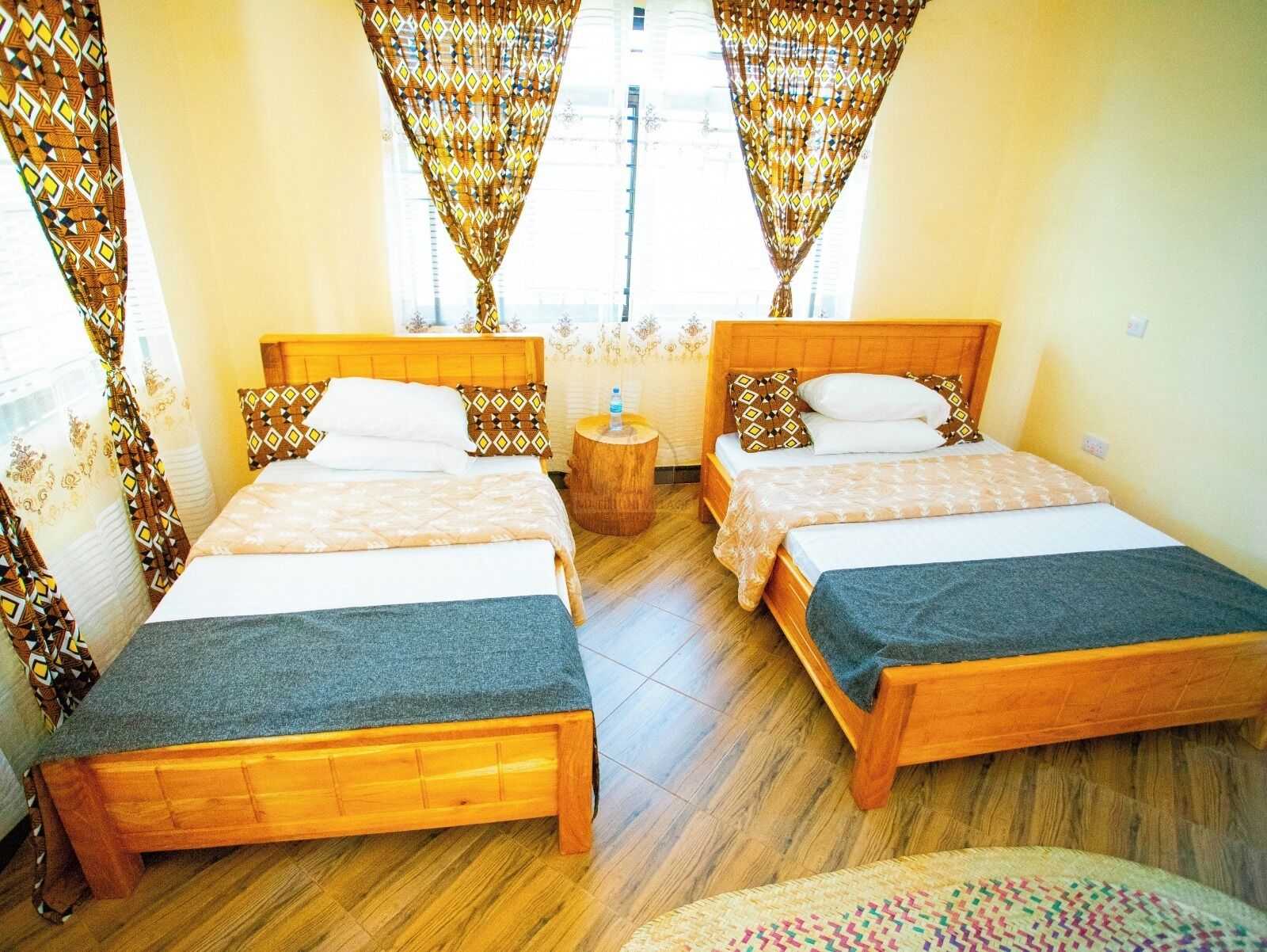 A hotel room with two wooden beds, a small wooden nightstand, and patterned curtains.