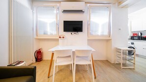 A small room with a white table and two chairs, a mounted TV, a radiator, and a fire extinguisher.