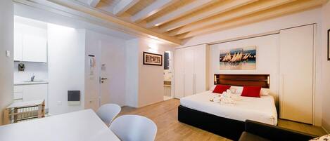 Habitación de hotel con cama, escritorio, sillas, una kitchenette pequeña y un cuadro en la pared.