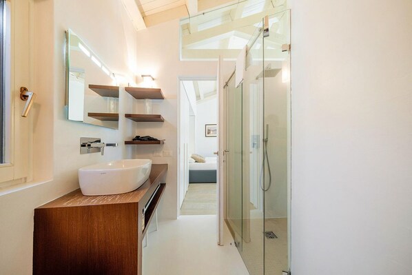 A modern bathroom with a large white sink, a mirror, and a glass-enclosed shower.