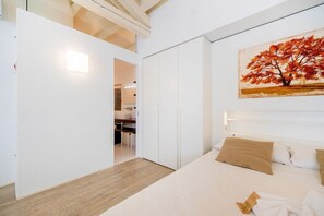 A bedroom with a bed, a painting, a wardrobe, and a bathroom visible through an open door.