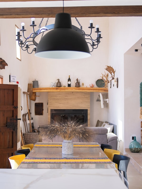 A dining area with a long table, chairs, a chandelier, a fireplace, and various decorative items. - Caseta Blanca : Complete Rural House in the mountain of Onil in Alicante (Onil)