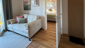 Ett modernt vardagsrum med en soffa, en matta och ett trägolv. Det finns en dörr som leder till ett annat rum.