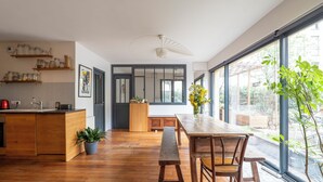 A modern kitchen with wooden cabinets, a dining area with a wooden table and bench, and large windows offering a view of the outdoors.