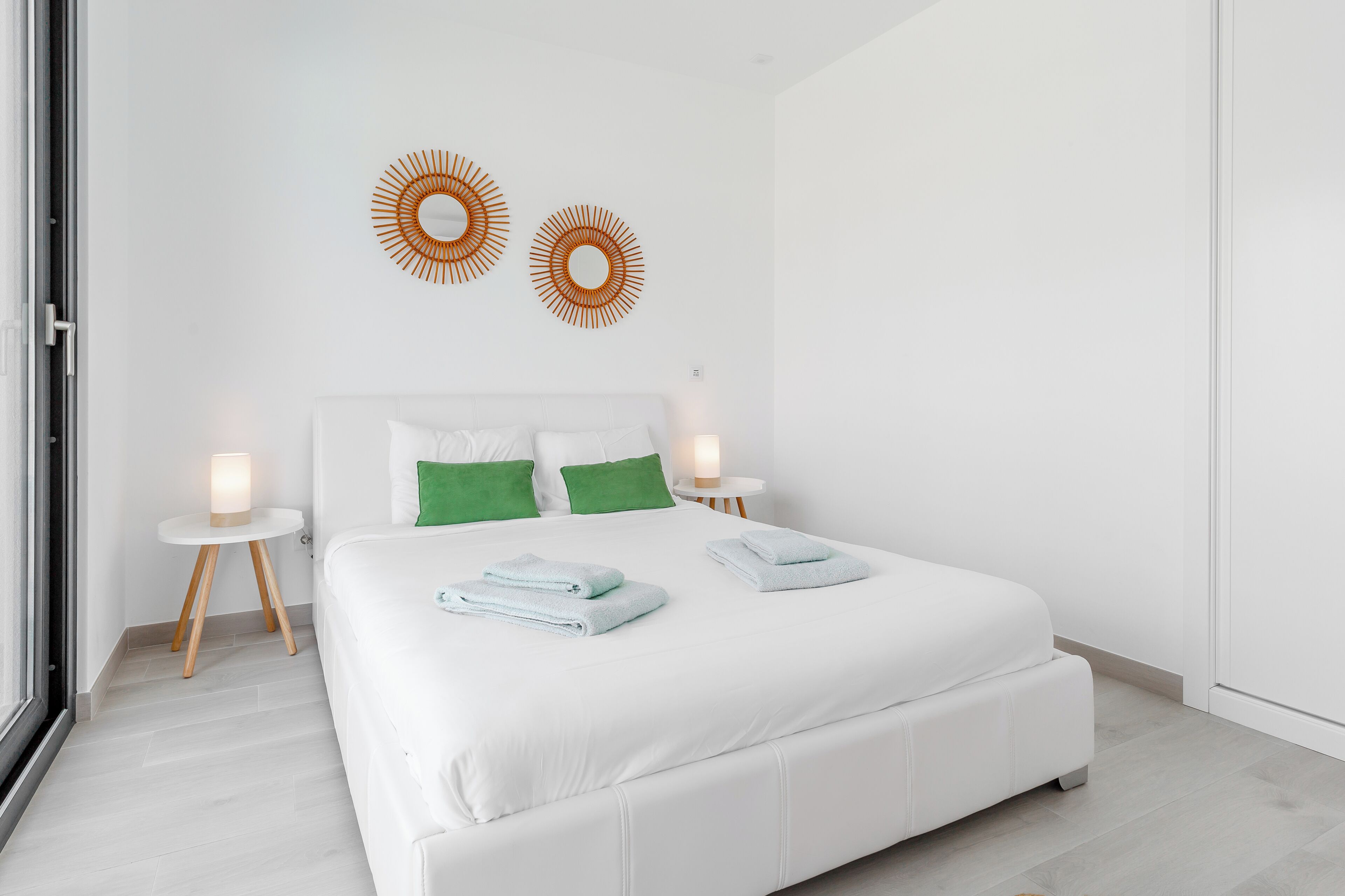 Ein modernes Schlafzimmer mit einem großen Bett, zwei Nachttischen und zwei dekorativen Wandspiegeln.