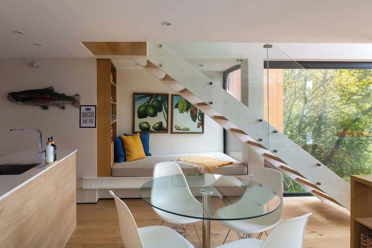 Un intérieur moderne avec une table en verre, des chaises blanches, un banc en bois et un escalier.