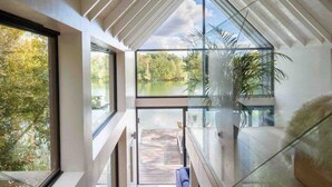 A modern interior with large glass windows, a wooden deck, and indoor plants. - The Boathouse - Romantic Glass Lodge - Hot Tub (South Cerney)