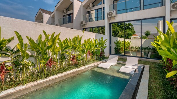A modern building with a swimming pool, surrounded by lush greenery and a clear blue sky. - U Villas Pandawa (Kutuh)