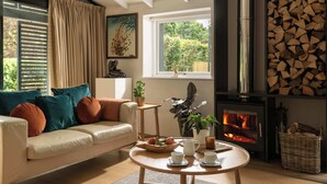 Ein gemütliches Wohnzimmer mit einer Couch, einem Couchtisch, einem Kamin und einem Fenster mit Blick auf Grünflächen.