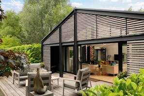 Une maison moderne dotée d’une terrasse, d’un espace salon extérieur et d’un intérieur visible, comprenant un canapé et un coin repas.
