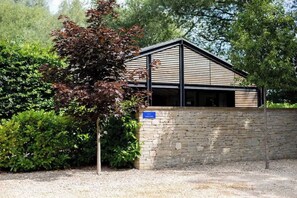 Un bâtiment moderne doté d’un toit en pente, entouré de verdure et bordé d’un mur de pierre.