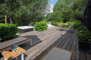 Une terrasse en bois avec des meubles d’extérieur, un jacuzzi et une végétation luxuriante.
