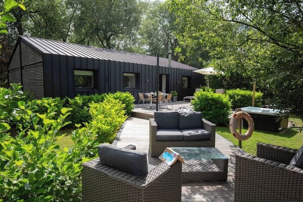 Un espace extérieur moderne, aménagé en patio, avec des meubles en osier, un jacuzzi et une structure métallique.
