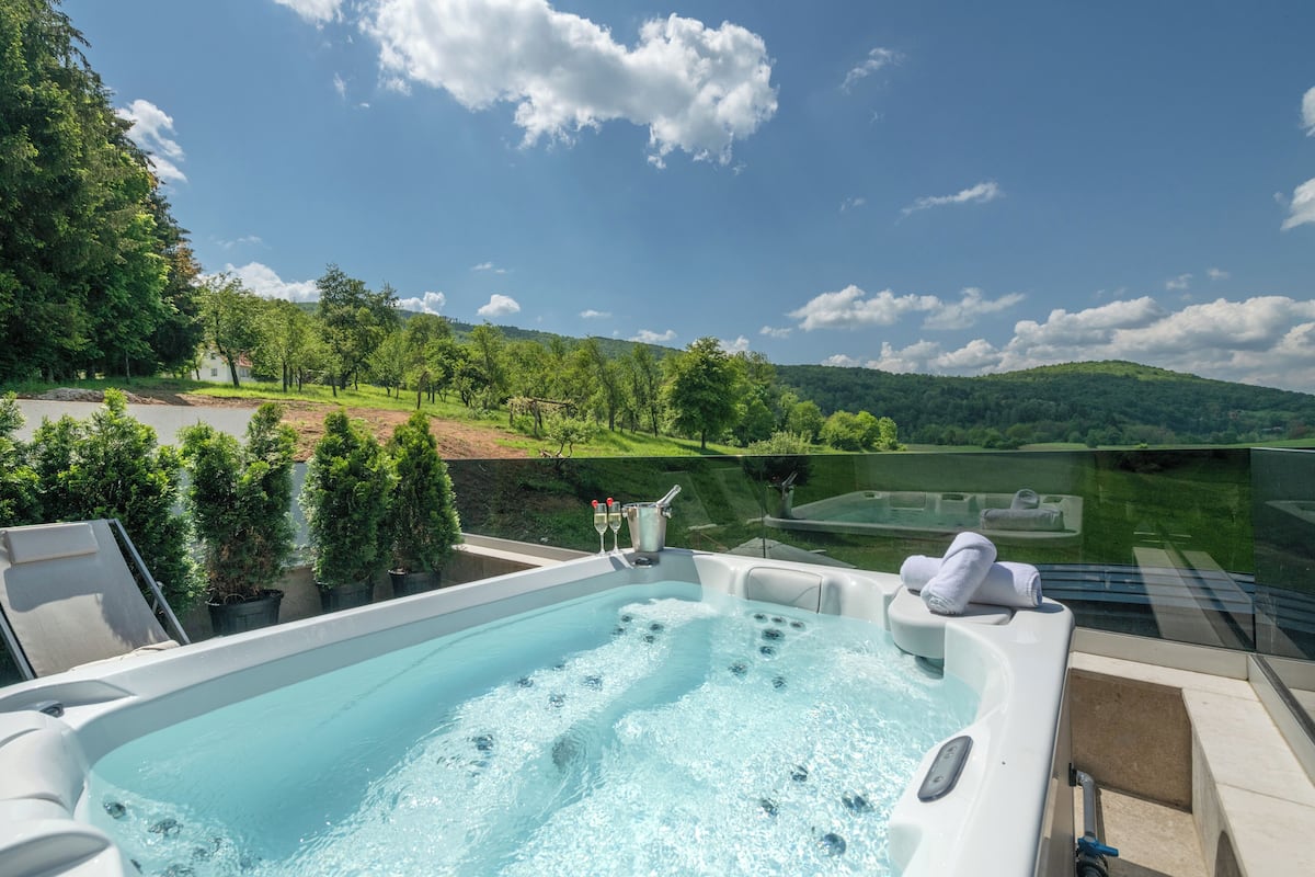 Un jacuzzi con barrera de vidrio, rodeado por un paisaje verde exuberante y un cielo despejado.