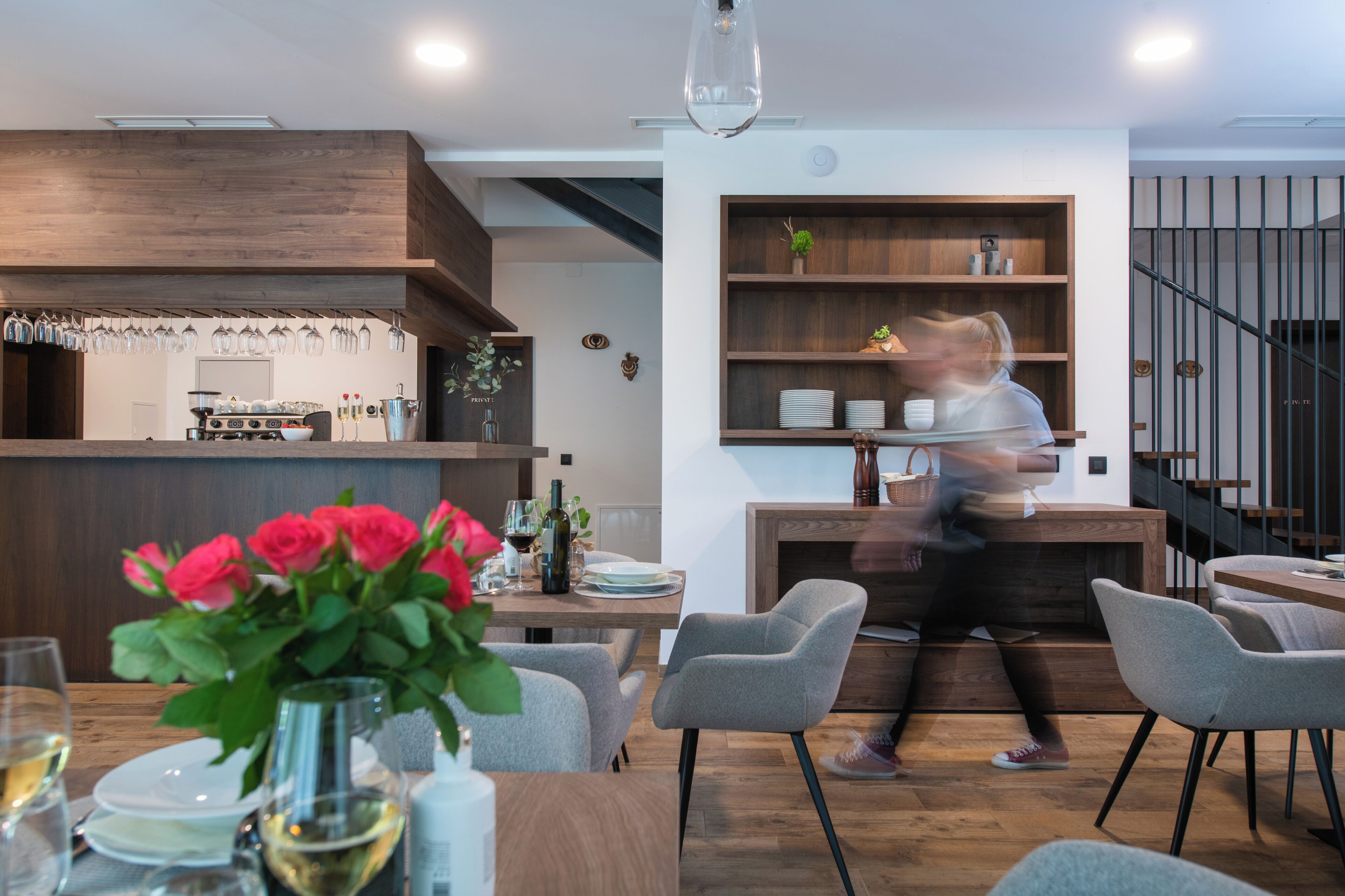 Un comedor moderno con una barra de madera, un florero de vidrio con flores y una escalera al fondo.