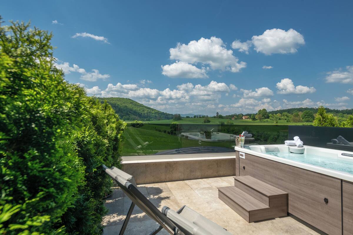 Un área de spa con un jacuzzi y asientos, con vistas a un paisaje verde y colinas.