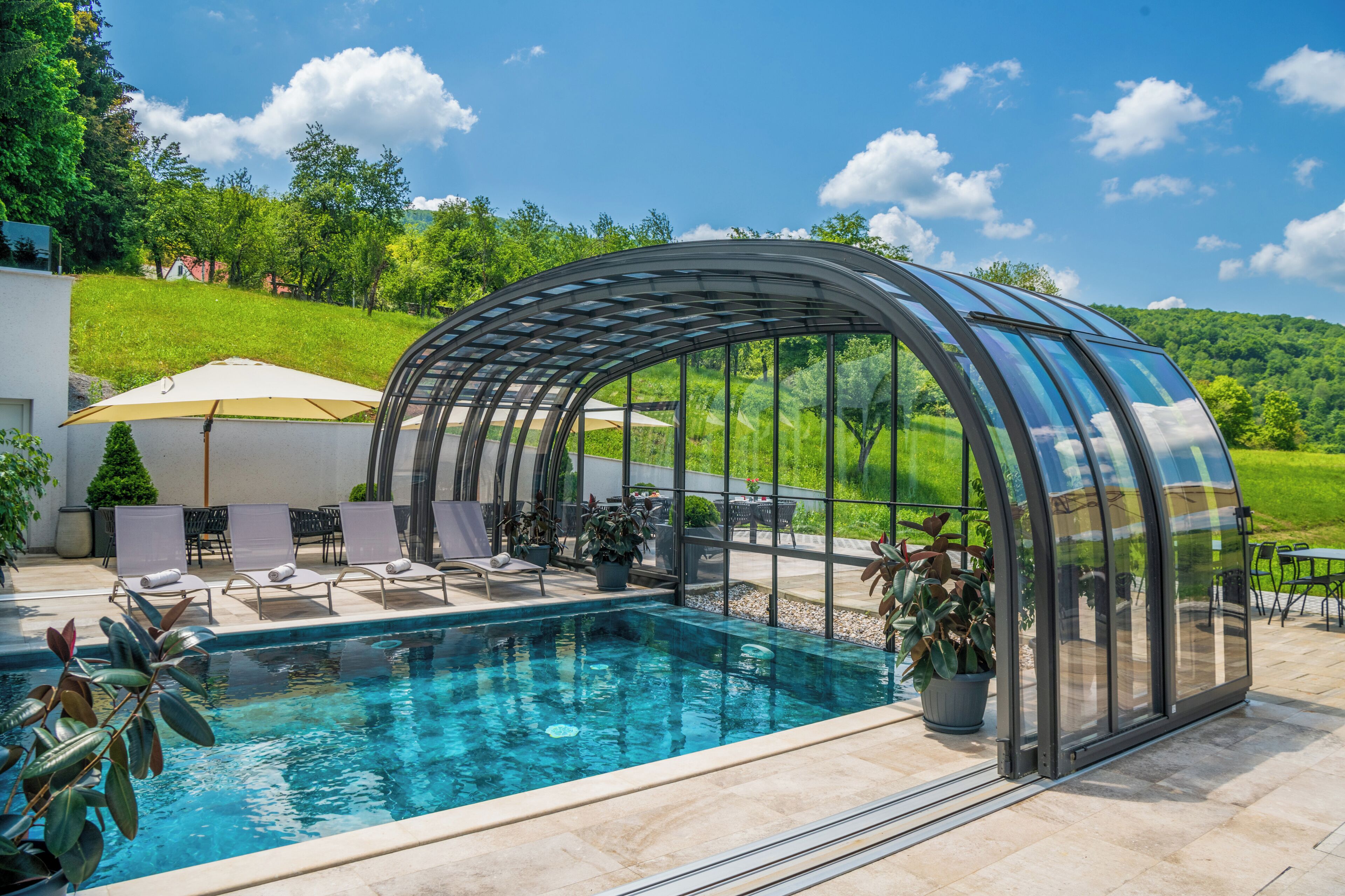 Un espace piscine entièrement vitré, doté de chaises longues et d’une pergola.