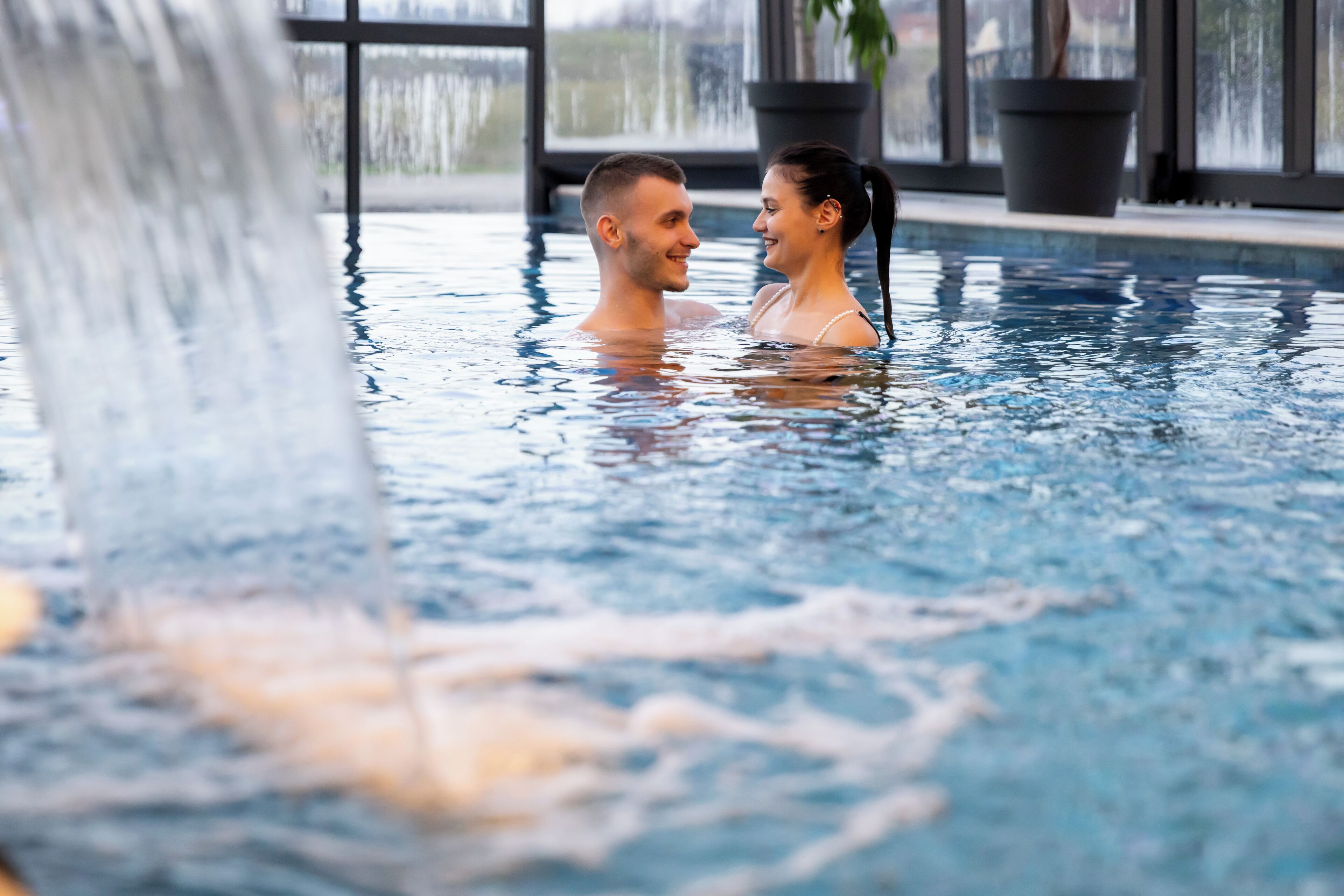 A couple in an indoor swimming pool with a waterfall feature.