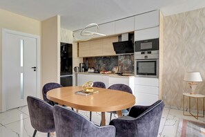 A modern kitchen with white cabinets, a black countertop, and a marble backsplash. There is a dining table with six chairs and a decorative gold ring on the table. - Angielska Grobla City Center by Lion Apartments (Gdansk)