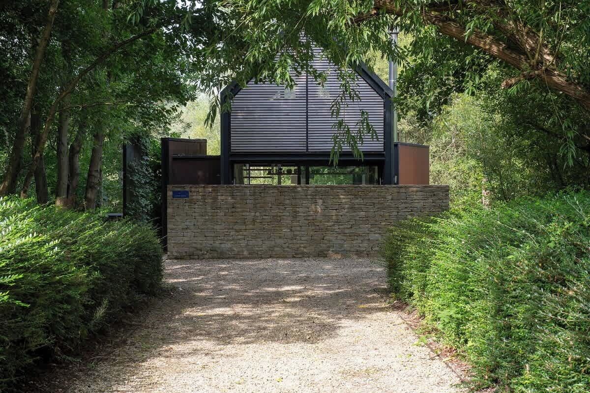 A modern building with a sloped roof, surrounded by dense greenery and a gravel path leading to the entrance.