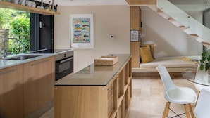 Una cocina moderna con horno empotrado, isla con encimera de vidrio y comedor con banco y sillas.