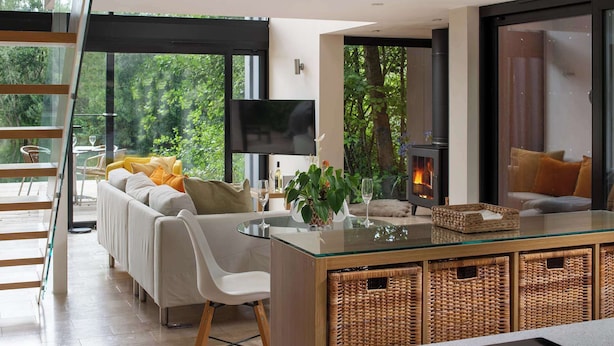 Una sala de estar moderna con una mesa de comedor de vidrio, sofás blancos, un televisor y una chimenea.