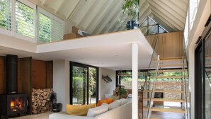 Un amplio salón con techo alto, chimenea, sofá con cojines y vistas a zonas verdes.