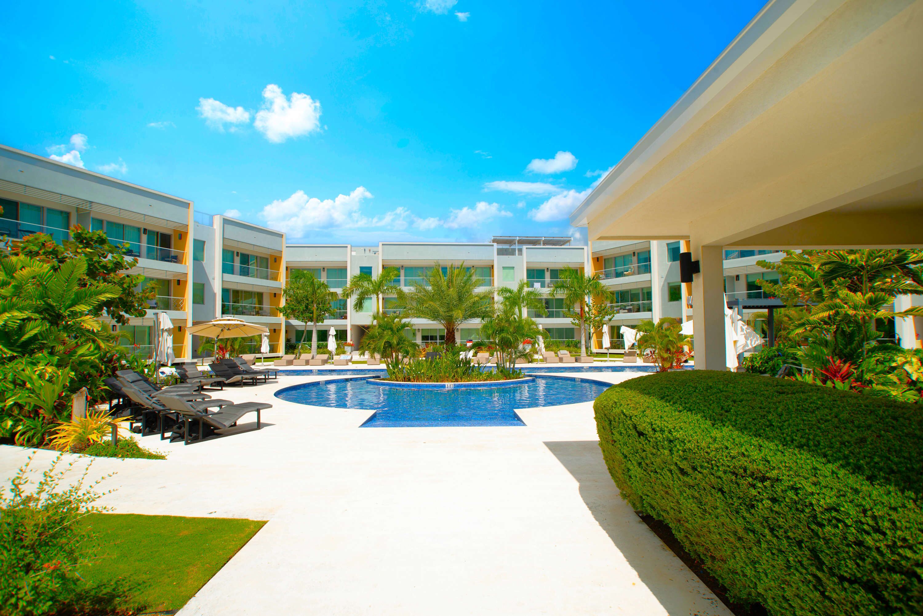 A modern hotel with a central pool, sun loungers, and lush landscaping.