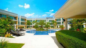 A modern hotel with a central pool, sun loungers, and lush landscaping.