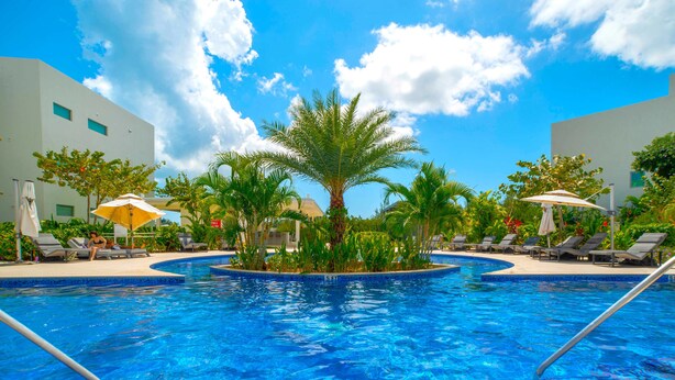 A swimming pool with lounge chairs and umbrellas, surrounded by palm trees and greenery. - Luxury Waterfront 3bed Penthouse w/Rooftop Terrace (George Town)