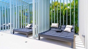 A modern outdoor seating area with two lounge chairs and a pergola structure, surrounded by lush greenery. - Luxury Waterfront 3bed Penthouse w/Rooftop Terrace (George Town)