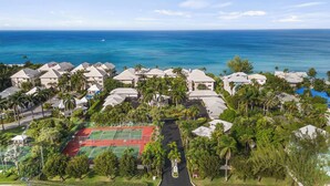 An aerial view of a coastal residential area with houses, a tennis court, and the ocean in the background.