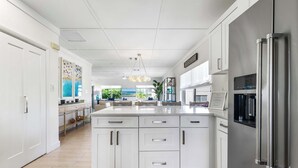 A modern kitchen with white cabinetry, a stainless steel refrigerator, and a large island with a built-in sink.