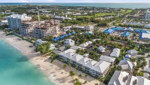 An aerial view of a coastal area with a beach, a large hotel under construction, and surrounding residential buildings.