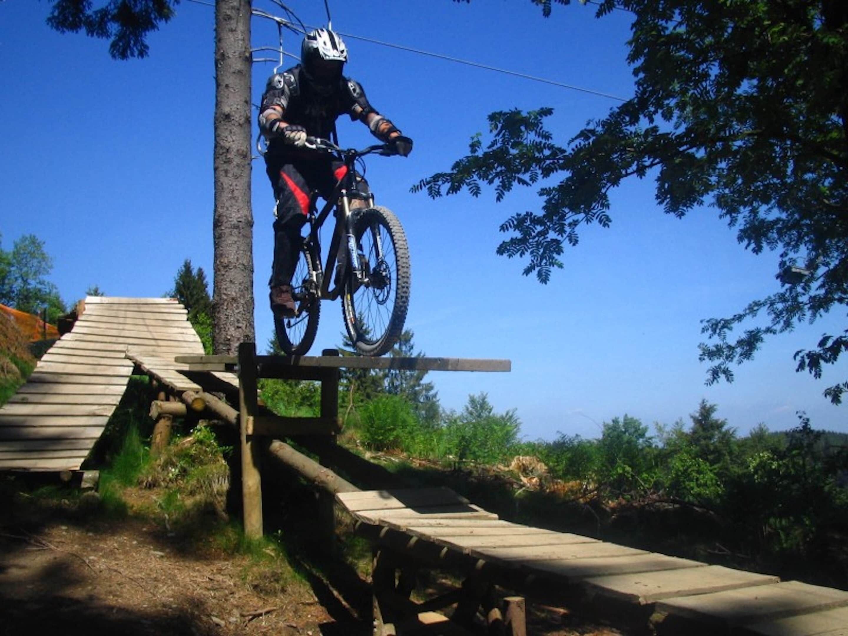 A mountain biker performing a jump over a wooden ramp.